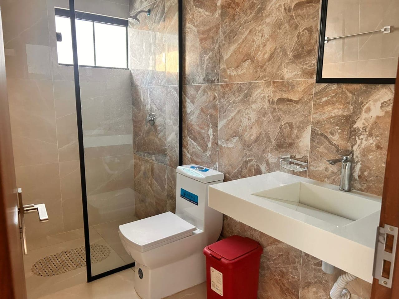 A marble-tiled bathroom with a glass-enclosed shower and floating sink
