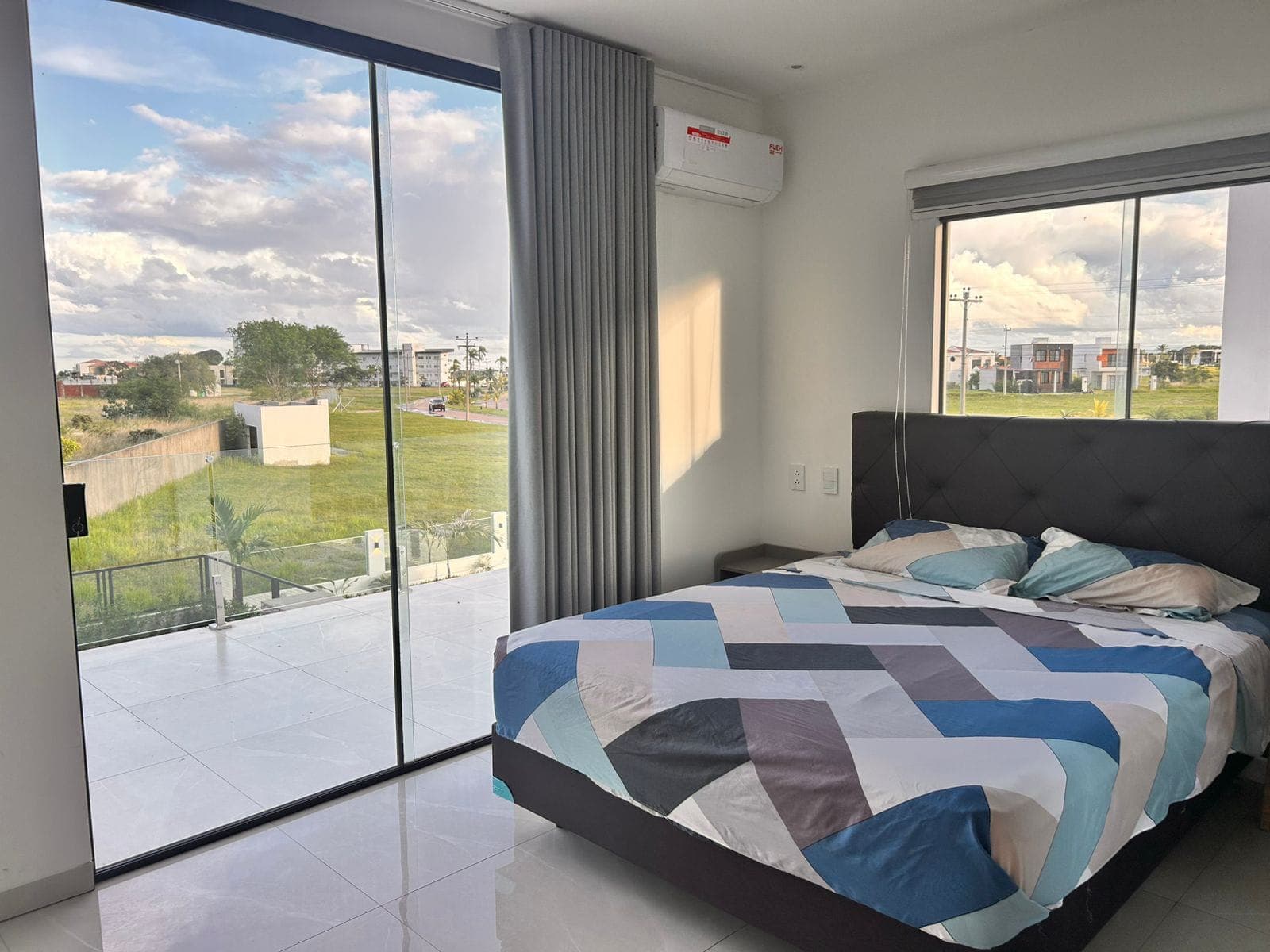 A bedroom with floor-to-ceiling windows, a private balcony, and a colorful bedspread